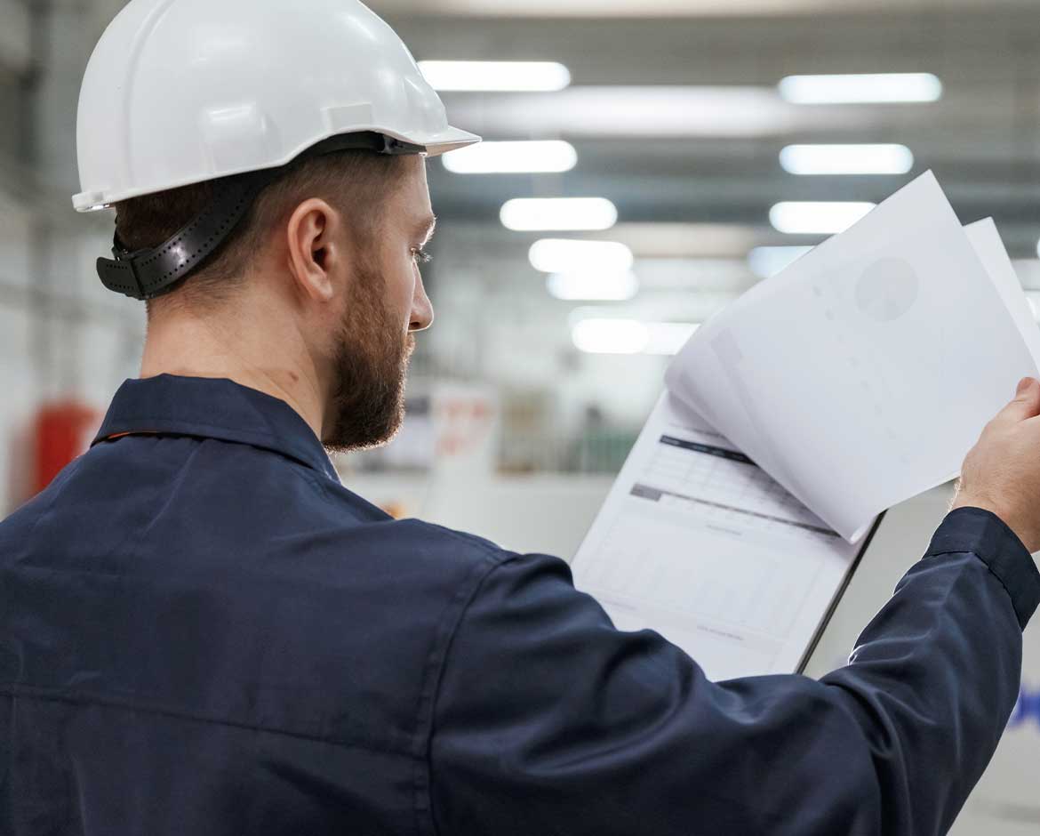 profissional-de-sst-de-capacete-visto-de-costas-analisando-os-documentos-do-pgr-dentro-da-fabrica
