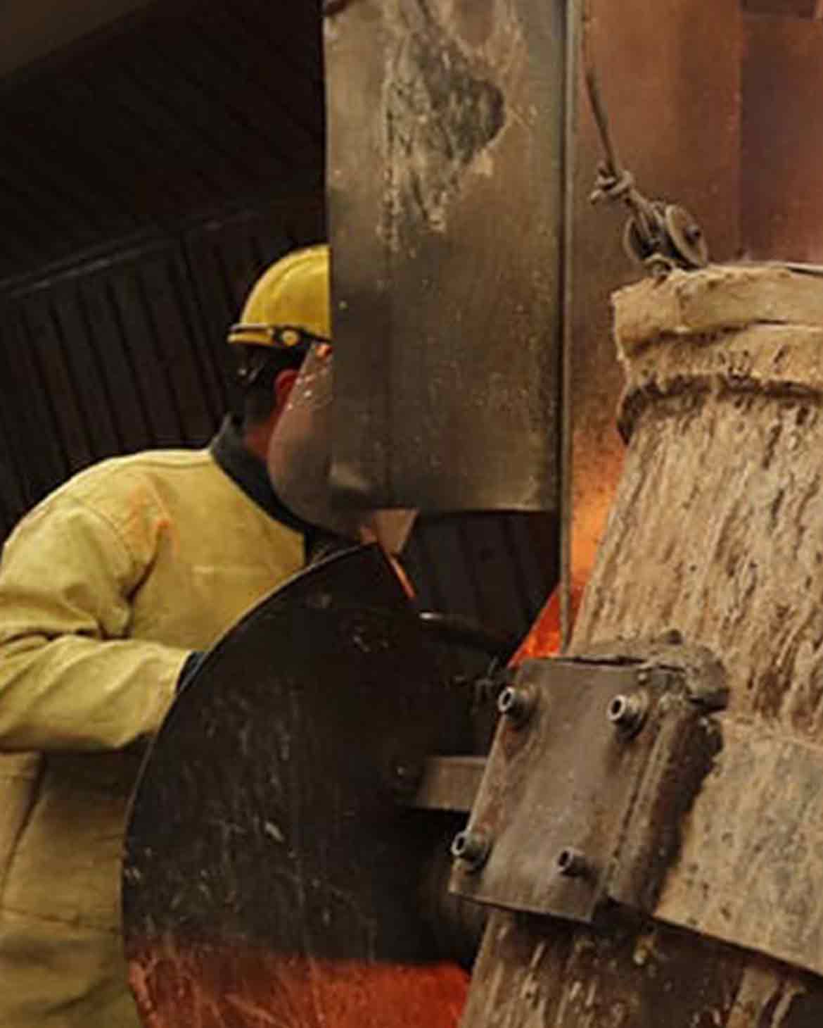 trabalhador industrial com capacete e avental de aramida operando equipamento com metal fundido incandescente