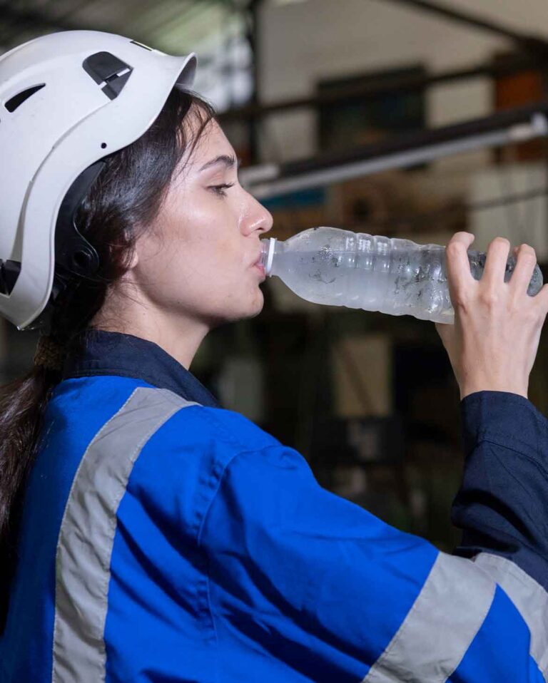 trabalhadora-industrial-com-capacete-de-segurança-exemplificando-a-gestão-de-calor-e-hidratação-ao-beber-água-para-combater-o-estresse-térmico
