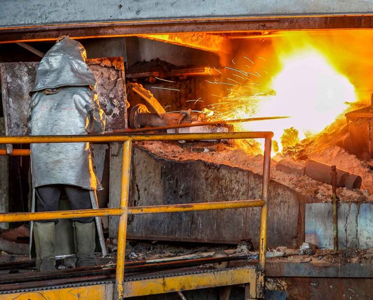 trabalhador em fundição usando vestimenta aluminizada completa como medida de controle para calor radiante na gestão de riscos térmicos.