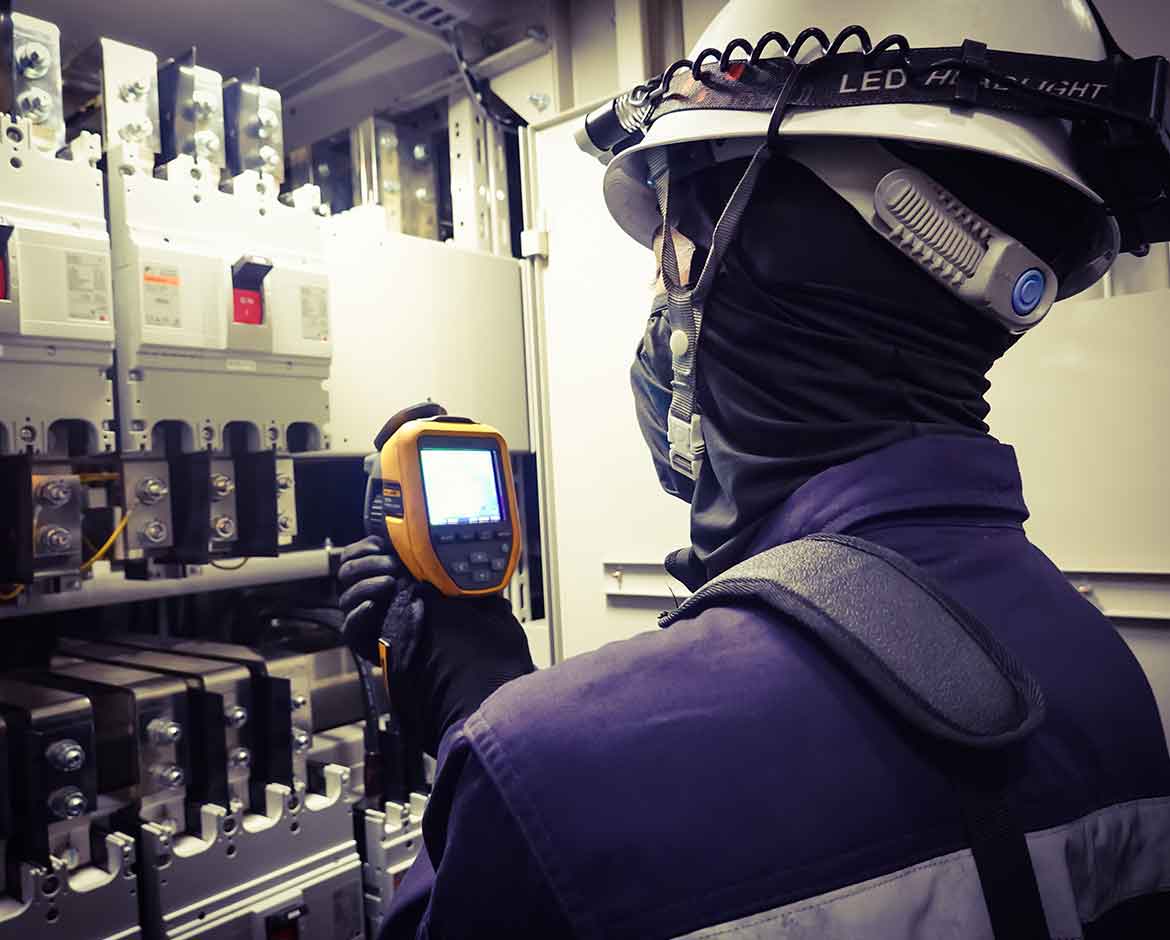 eletricista com balaclava antichama e capacete inspecionando painel eletrico com termovisor para ilustrar o que e atpv na prevencao de arco eletrico
