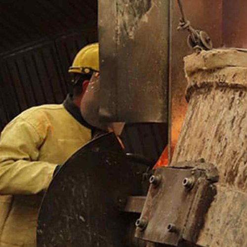trabalhador industrial com capacete e avental de aramida operando equipamento com metal fundido incandescente