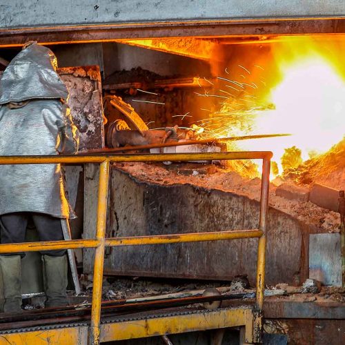 trabalhador em fundição usando vestimenta aluminizada completa como medida de controle para calor radiante na gestão de riscos térmicos.