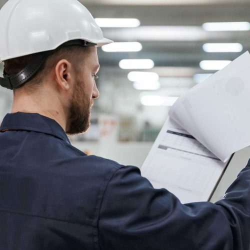 profissional-de-sst-de-capacete-visto-de-costas-analisando-os-documentos-do-pgr-dentro-da-fabrica