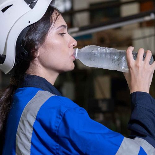 trabalhadora-industrial-com-capacete-de-segurança-exemplificando-a-gestão-de-calor-e-hidratação-ao-beber-água-para-combater-o-estresse-térmico